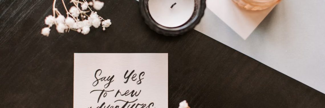 Flat lay of a motivational note with candles and flowers on a wooden surface.